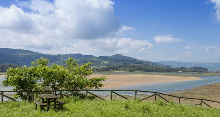 Zone herbeuse avec une table de pique-nique donnant sur une rivière et des collines sous un ciel nuageux.