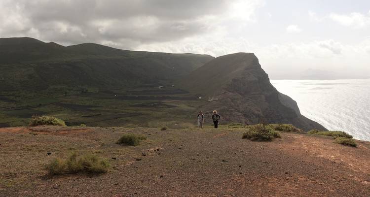 Two people on a hill overlooking the sea with clouds in the sky.