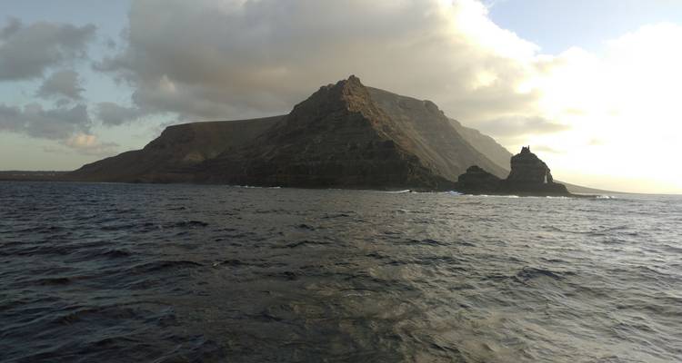 Formación montañosa rocosa que se alza desde el mar bajo cielos nublados.