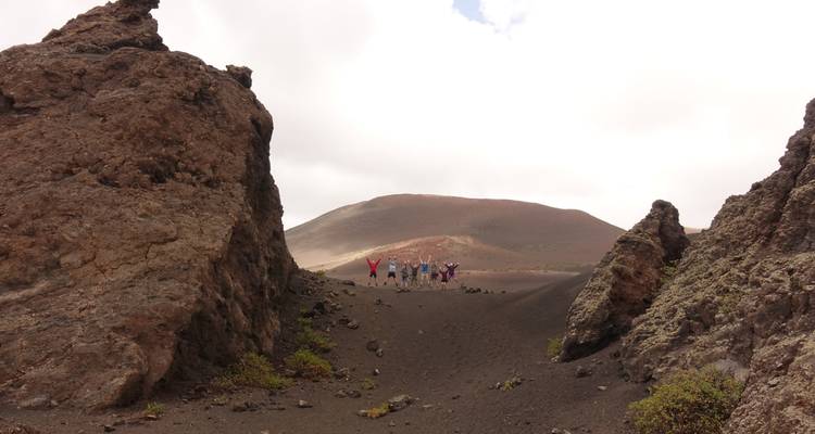 Pequeño grupo de excursionistas de pie entre formaciones rocosas volcánicas oscuras en un paisaje árido cubierto de ceniza.