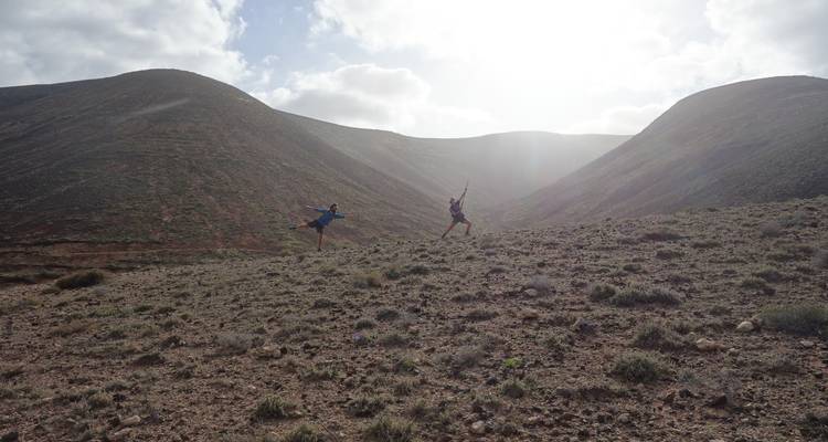 Two people leaping with joy on a barren landscape with hills in the background.