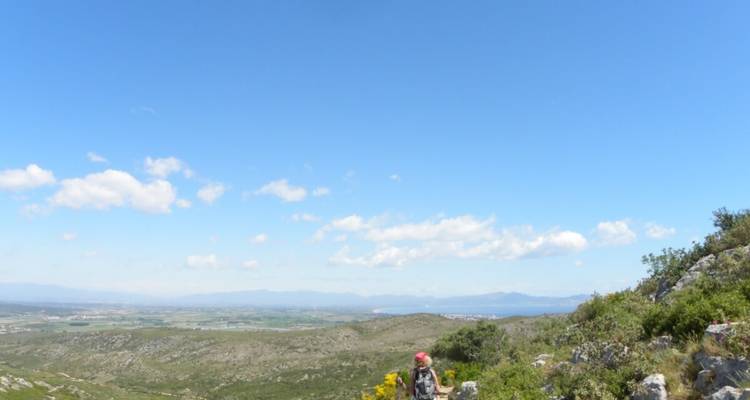 Hiker in a vast mountainous landscape under a blue sky.
