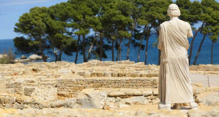 Ruines anciennes avec une statue et vue sur la mer.