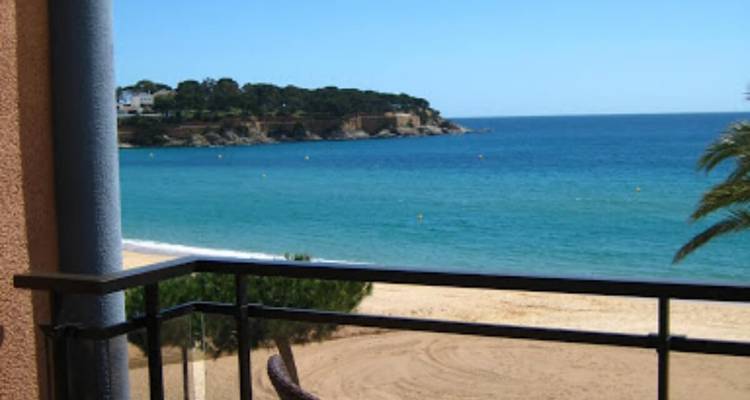 Vue depuis un balcon sur une plage et une mer bleue.