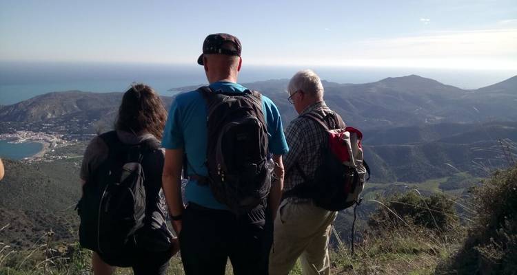 Trois personnes debout sur une colline avec une vue sur la mer et les montagnes.