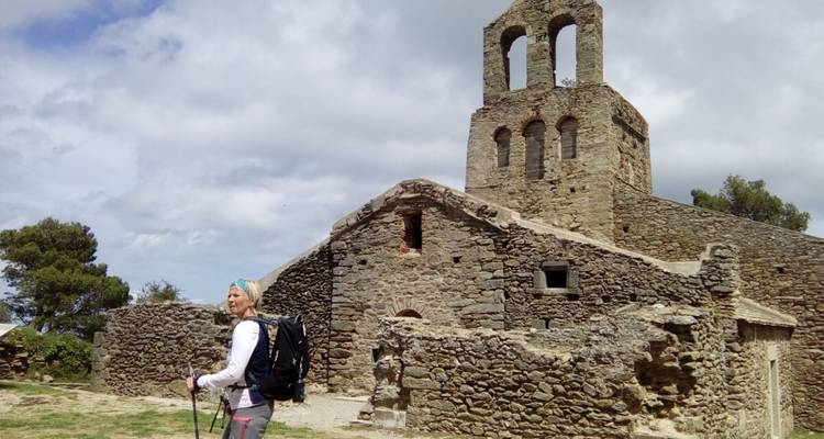 Bâtiment en pierre avec un clocher et une femme en randonnée avec un sac à dos.