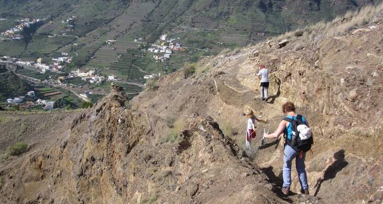Randonneurs sur un sentier de montagne étroit et escarpé avec un village au loin.