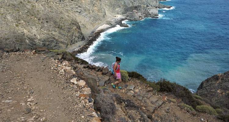 Femme marchant le long d'un sentier côtier rocheux avec vue sur l'océan.