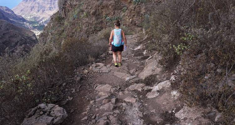 Femme descendant un sentier rocheux de montagne.