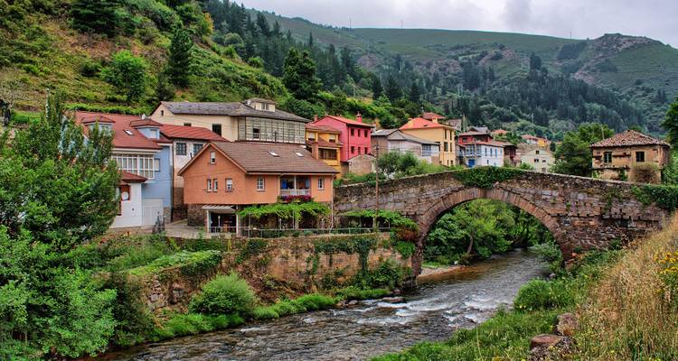 Eine malerische Dorfszene mit bunten Häusern und einer Steinbrücke über einem Fluss.
