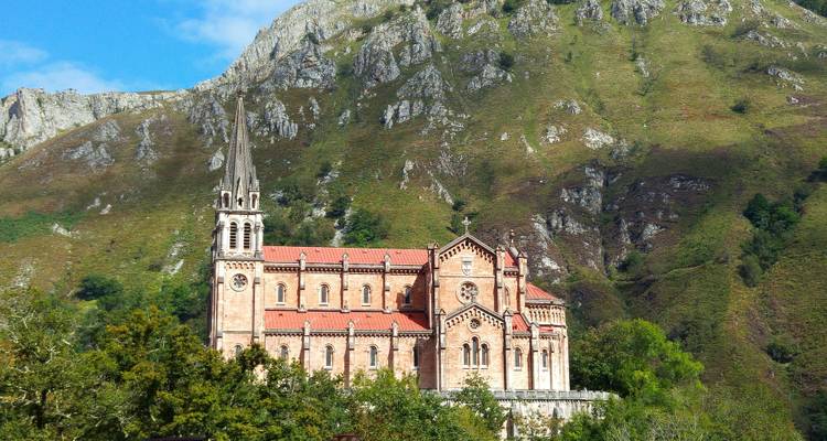 Eine historische Kirche auf einem Hügel mit bergiger Kulisse unter klarem Himmel.