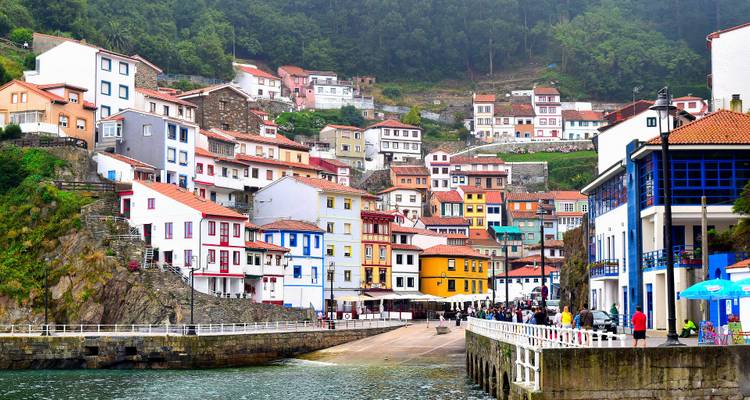 Eine Küstengemeinde mit bunten Häusern am Wasser, Menschen sind auf der Straße sichtbar.