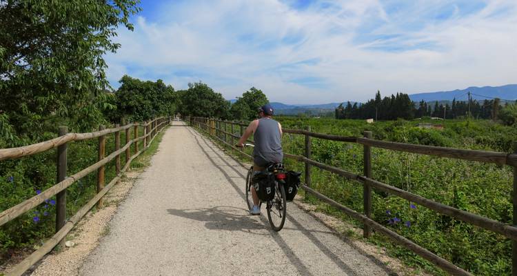 Radfahrer auf einem ländlichen Weg mit Grün und Bergen in der Ferne.