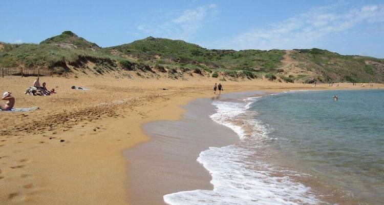 Plage de sable avec des vagues douces et des collines vertes.