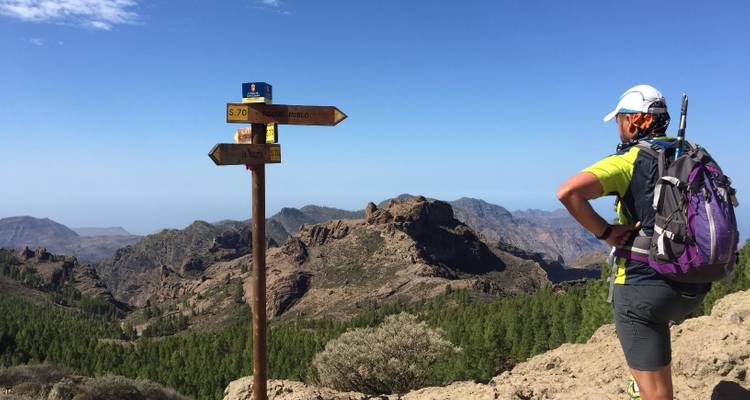Randonneur debout près de panneaux directionnels avec des montagnes en arrière-plan.