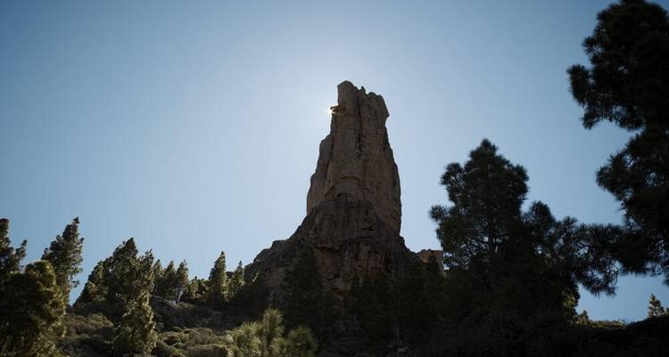 Pinacle rocheux rétroéclairé par le soleil avec des arbres à la base.