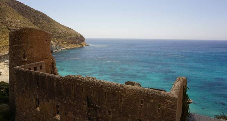 Ruines au bord de la mer avec un décor montagneux en arrière-plan.