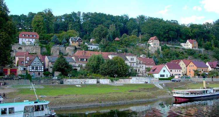 Village au bord de la rivière avec des maisons colorées et des bateaux amarrés le long du rivage.
