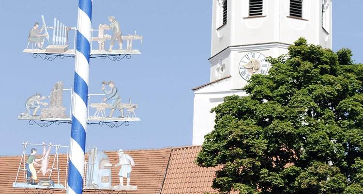 Mât de mai décoratif et un clocher d'église sous un ciel lumineux.
