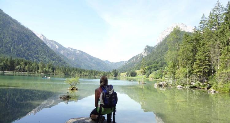 A person sitting by a calm lake, surrounded by mountains.