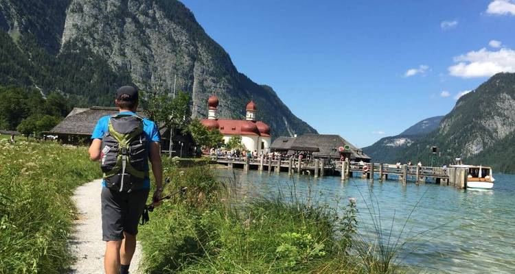 A person walking along a lakeside path towards a picturesque church.