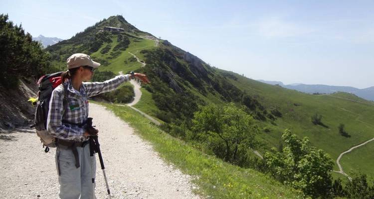 A person pointing towards a hilly landscape with distant mountain views.