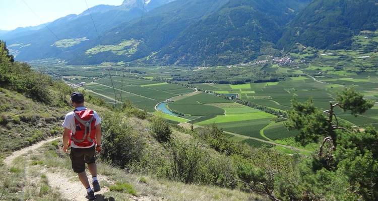 Una persona caminando con un valle de campos y montañas.