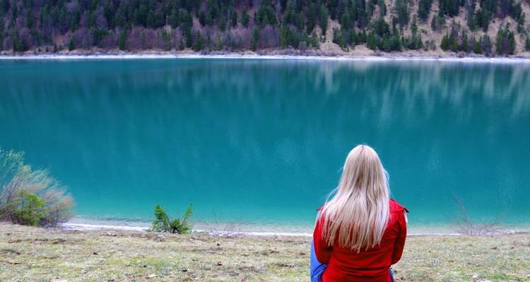 Vrouw zittend bij een turkooise meer omringd door bossen.
