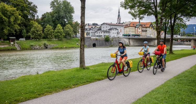 Fietsers volgen het pad langs de rivier voorbij een historisch Beiers stadje met kerktoren en gewelfde brug.
