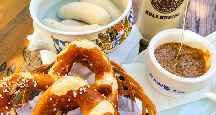 Traditionele Beierse snack van pretzels, witte worstjes in keramische pot, zoete mosterd en bierpul op houten tafel.