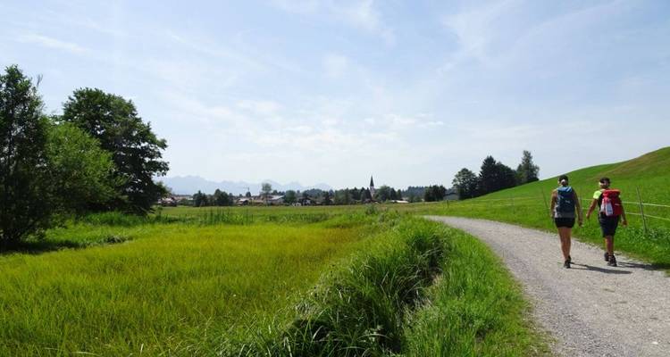 Deux personnes marchant sur un sentier rural avec des montagnes en arrière-plan.
