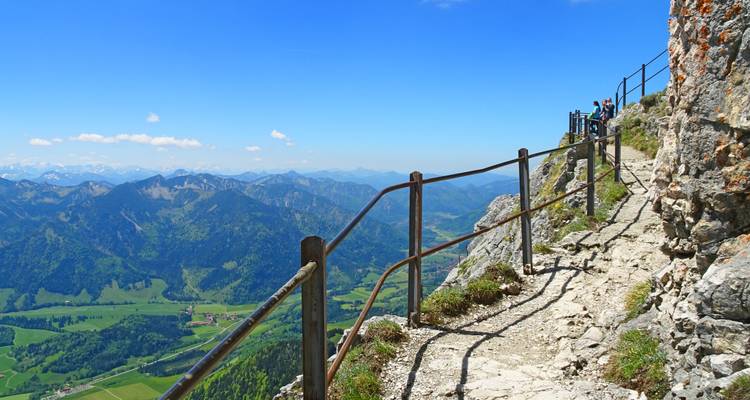 Een smal pad langs de rotswand met leuningen biedt uitgestrekte uitzichten over valleien en verre bergketens.