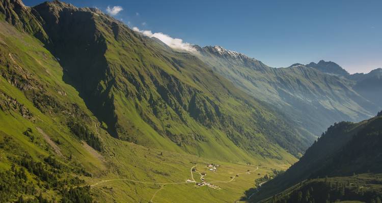 Talblick umgeben von hohen, schroffen Bergen unter einem klaren Himmel.