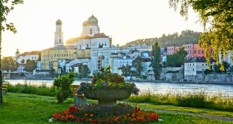 Malerische Aussicht auf eine Stadt am Fluss mit Blumen im Vordergrund.