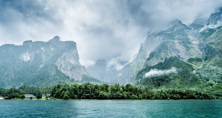 Paisaje montañoso de lago con nubes ondulantes.