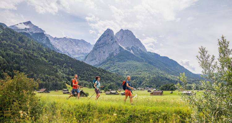 Wandelaars steken grasachtige vallei over met dramatische alpentoppen en verspreide boerderijen.
