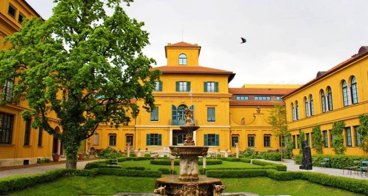 Geel historisch gebouw met een fontein op de voorgrond.