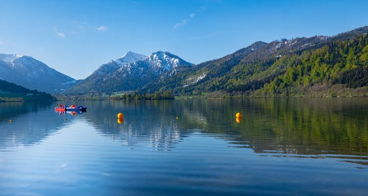 Ein klarer Bergsee mit Booten und schneebedeckten Bergen im Hintergrund.