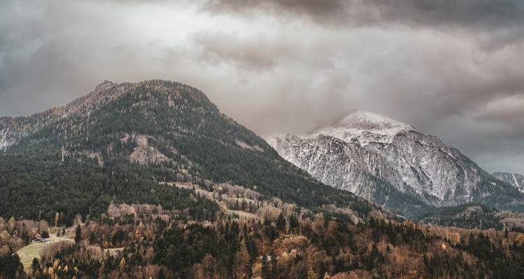 Mountain peaks partially covered with snow and surrounded by dense forests.