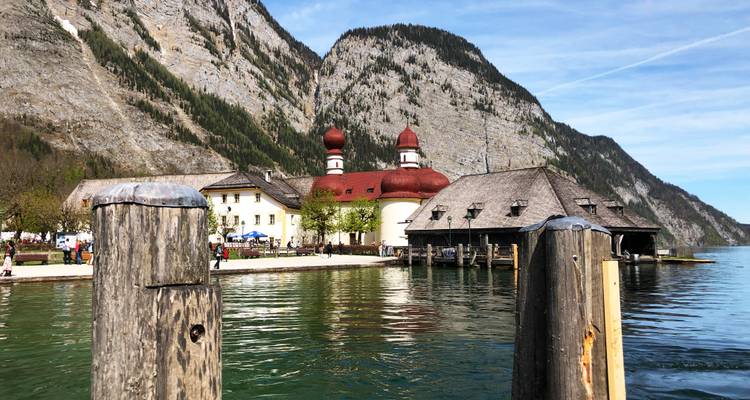 Église St. Bartholomä au bord d'un lac avec un arrière-plan montagneux.