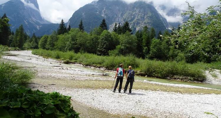 Twee wandelaars bij een rivier met bergen.