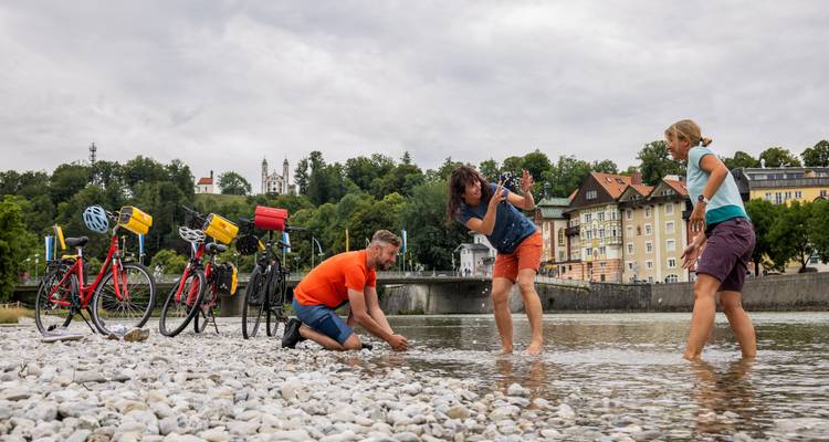 Grupo de ciclistas jugando en las aguas poco profundas de un río junto a sus bicicletas estacionadas en el pueblo