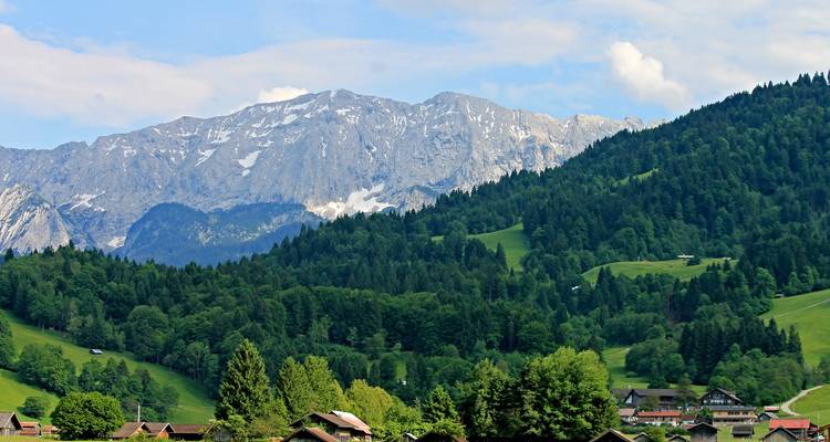 Alpenlandschaft mit grünen Wiesen und schneebedeckten Bergen.