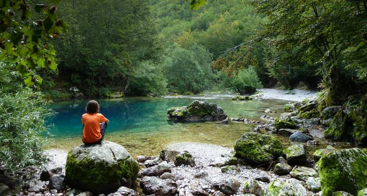 Person, die an einem klaren Fluss sitzt, umgeben von Wald.