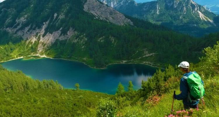 Randonneur avec un sac à dos vert regardant un lac entouré de montagnes.