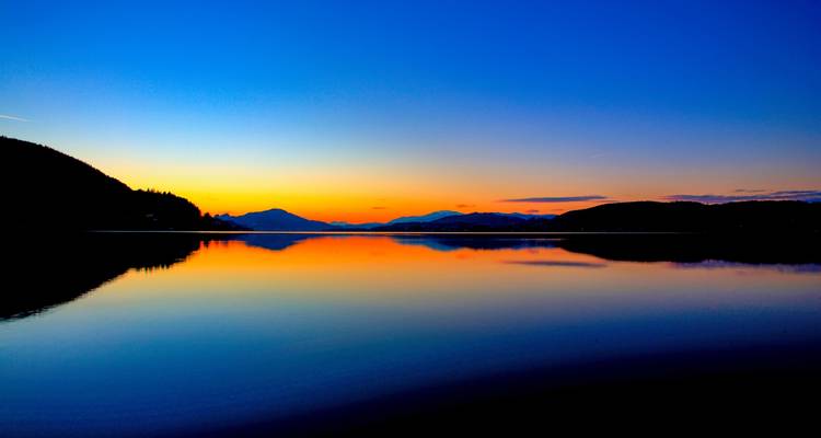 Ein lebendiger Sonnenuntergang über einem ruhigen See, der die Farben des Himmels widerspiegelt.