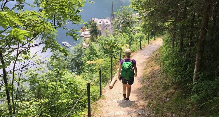 Un randonneur marchant sur un sentier avec vue sur un lac et un clocher d'église en contrebas.