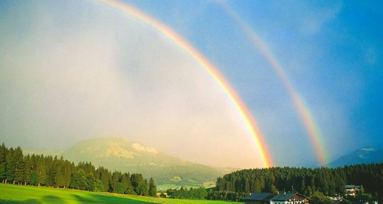 Dubbele regenboog boven een groen landschap.
