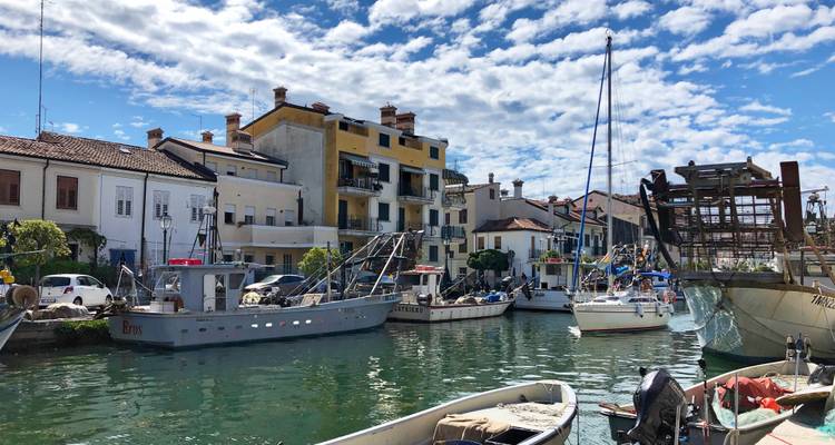 Fischerboote und pastellfarbene Häuser säumen einen ruhigen Kanal unter einem wolkengesprenkelten Himmel.