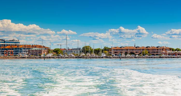 Eine Küstenstadt und Marina vom Wasser aus gesehen mit Kielwasser im Vordergrund an einem klaren Tag.